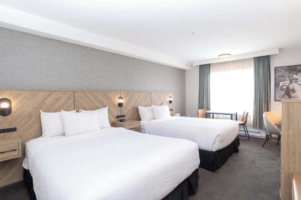 A hotel room with two beds, a small table, a chair, and a desk.