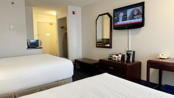 Habitación de hotel con dos camas, un televisor montado en la pared, un escritorio con teléfono y cafetera, y un espejo sobre el escritorio.
