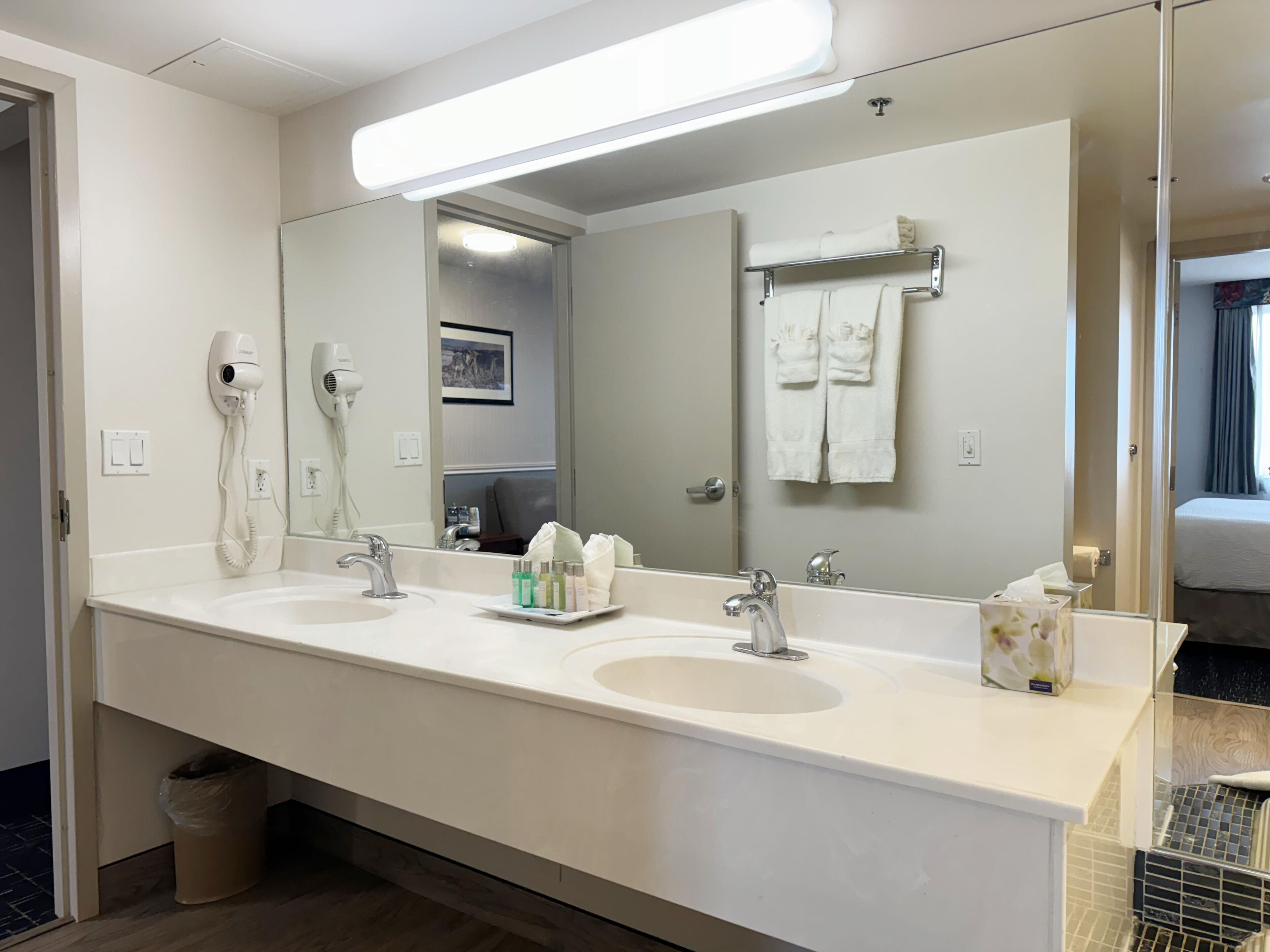 A hotel bathroom with two sinks, a large mirror, and a towel rack.