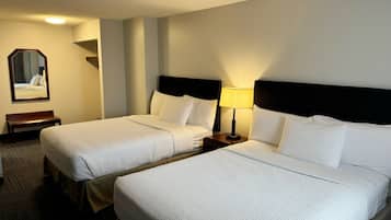Una habitación de hotel con dos camas, una mesita de noche con lámpara, un banco y un espejo en la pared.