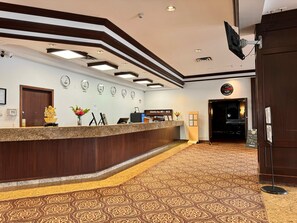 A reception area with a wooden reception desk, a clock, and a sign for the Italian restaurant lounge. - Divya Sutra Plaza and Conference Centre Calgary Airport (Calgary)