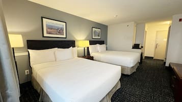 A hotel room with two beds, a headboard, a nightstand, a lamp, and a framed picture on the wall.