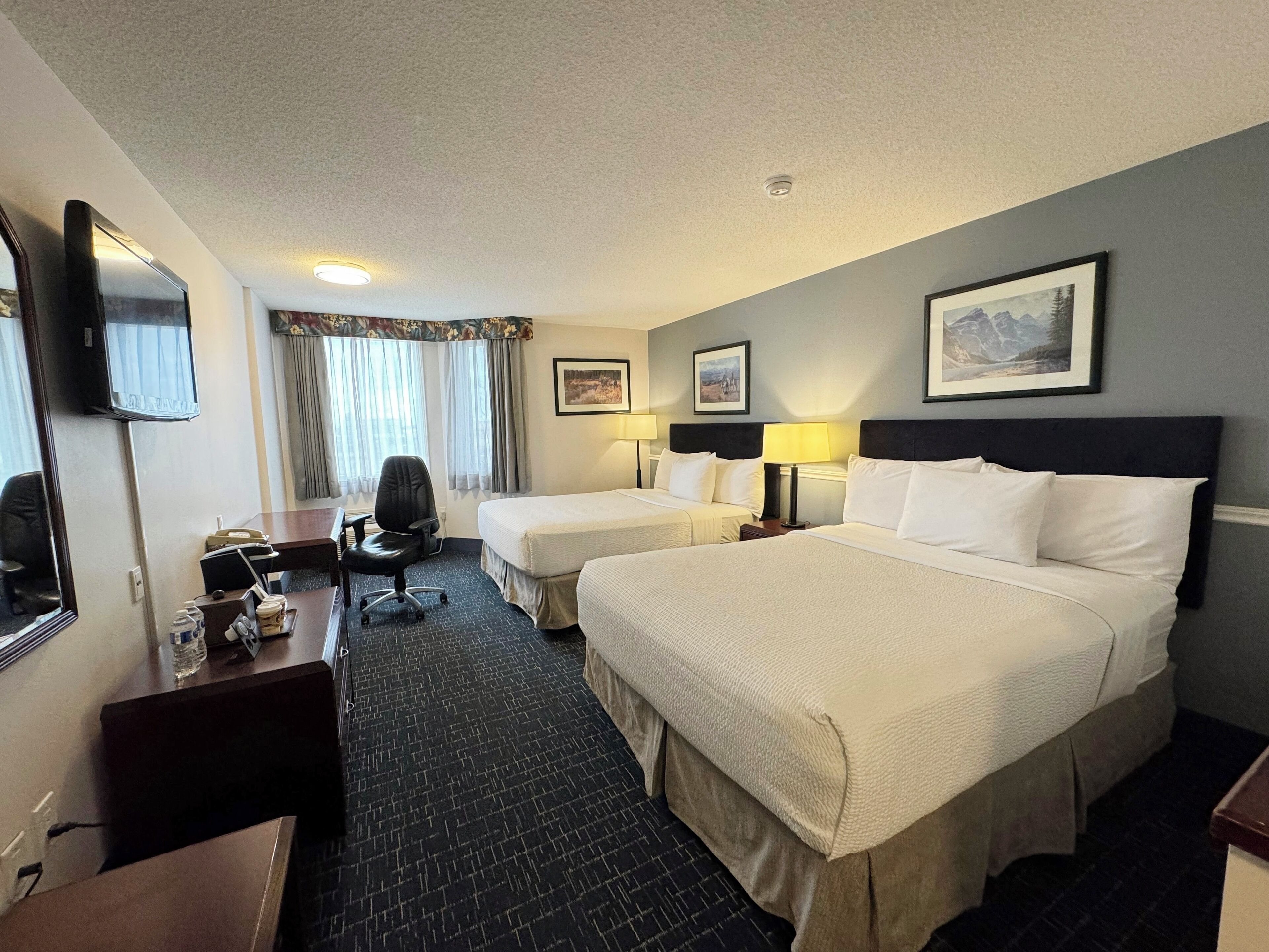 A hotel room with two beds, a desk, a chair, a television, and a window with curtains.