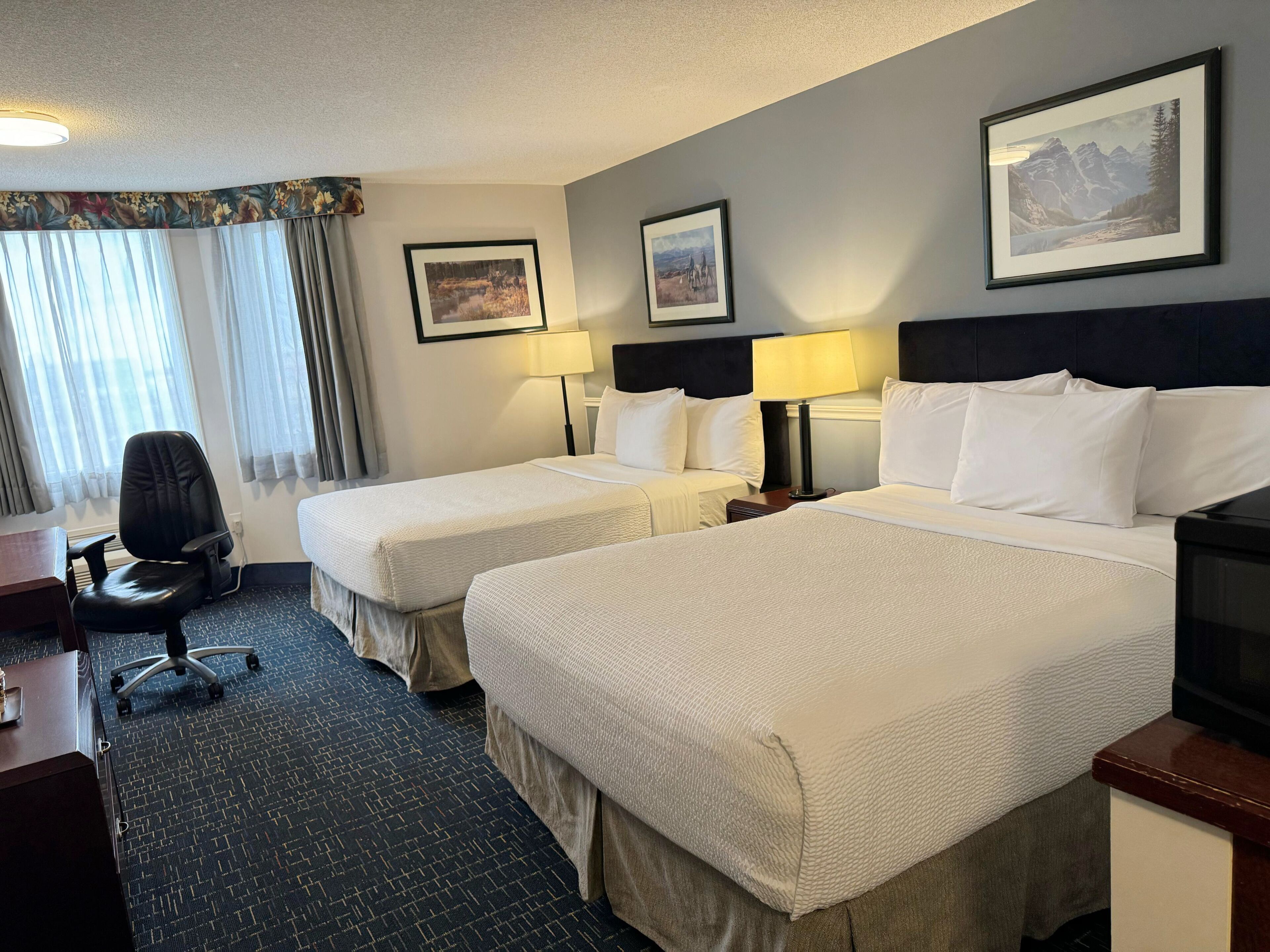 A hotel room with two beds, a desk, a chair, and a TV.