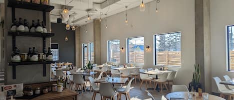 A spacious restaurant with high ceilings, exposed ductwork, and large windows offering views of the outside.
