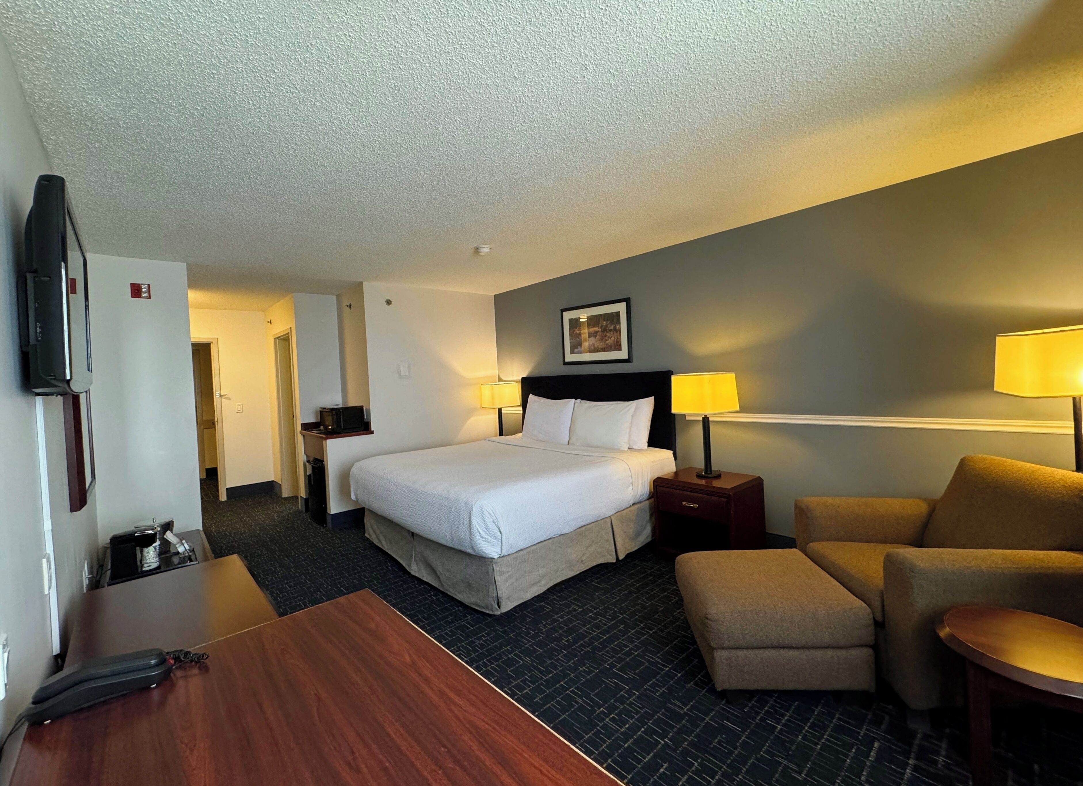 A hotel room with a bed, bedside tables, a desk, a chair, and a television.