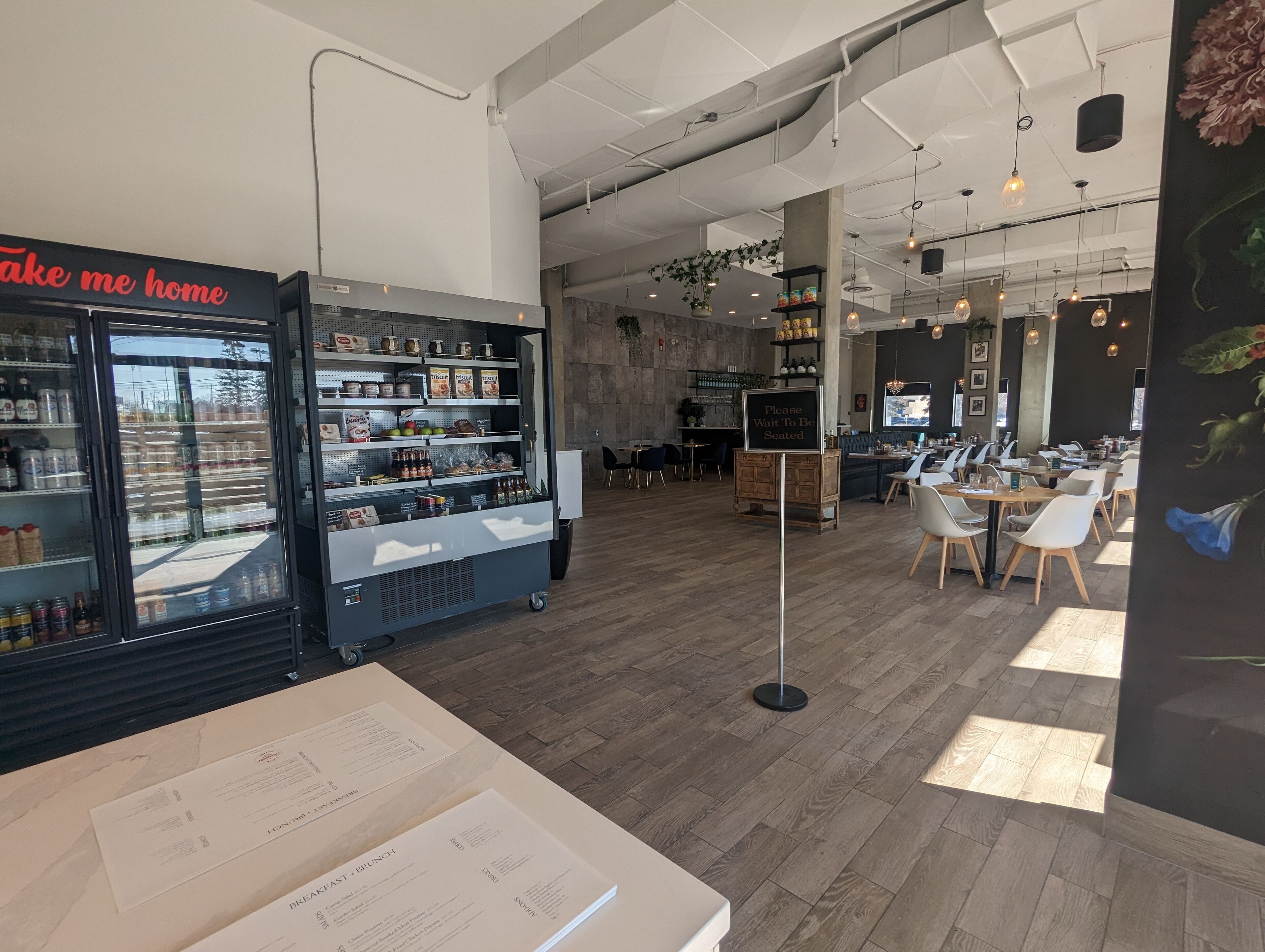 A cafe interior with a refrigerated display case, wooden tables, and a menu stand.