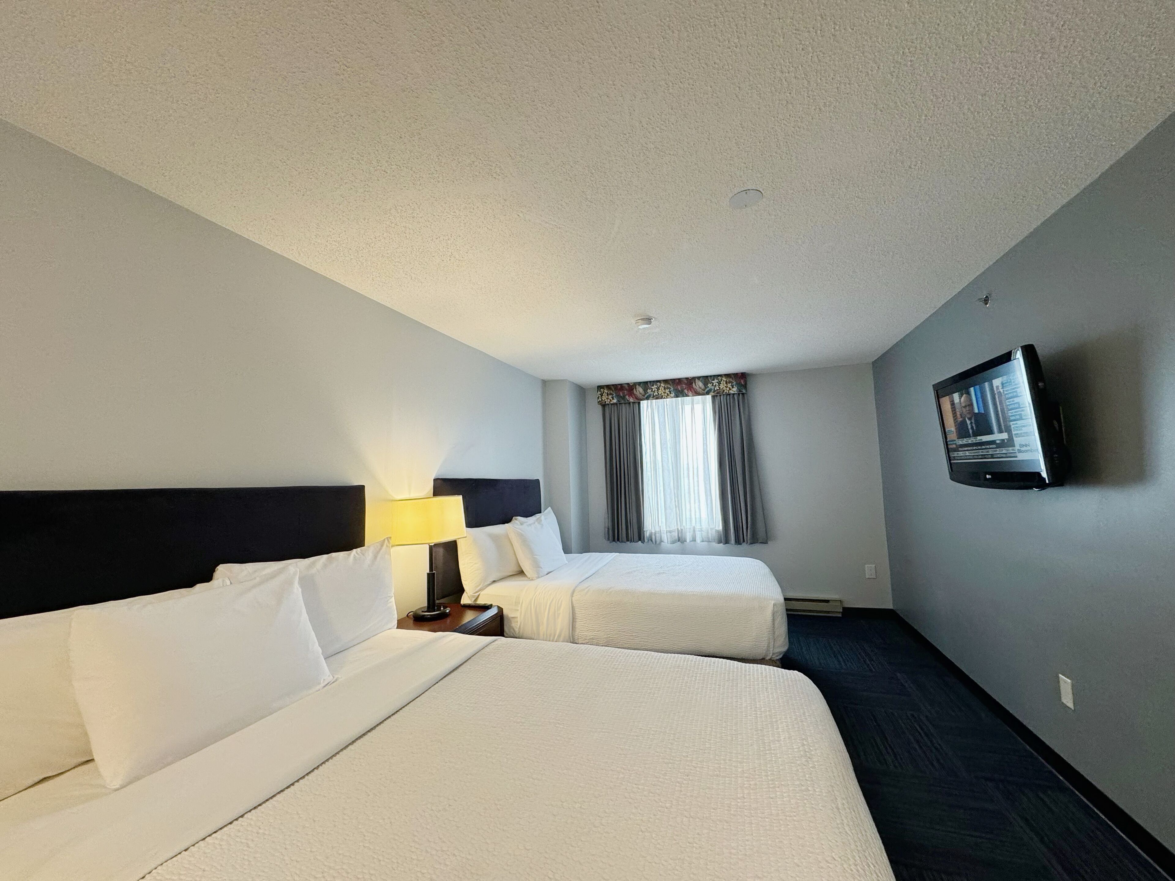 A hotel room with two beds, a TV on the wall, and a window with curtains.