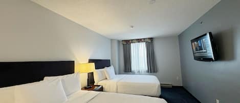 A hotel room with two beds, a TV on the wall, and a window with curtains.