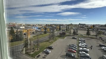 Un estacionamiento con varios autos, un edificio con un letrero azul, y un cielo despejado con nubes.