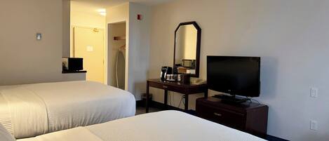 Habitación de hotel con dos camas, un escritorio con televisión y un espejo.