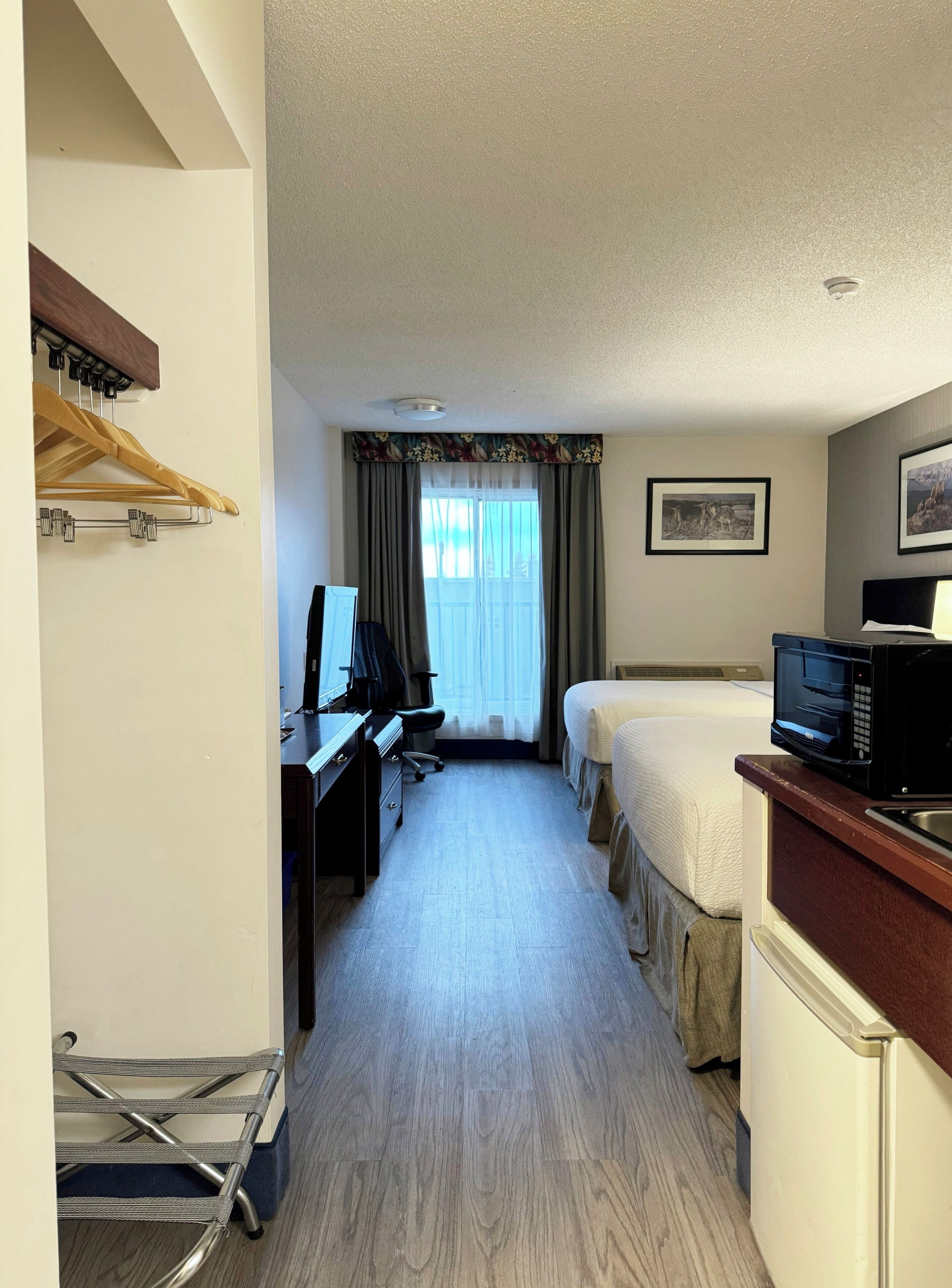 A hotel room with a desk, computer, bed, and kitchenette.