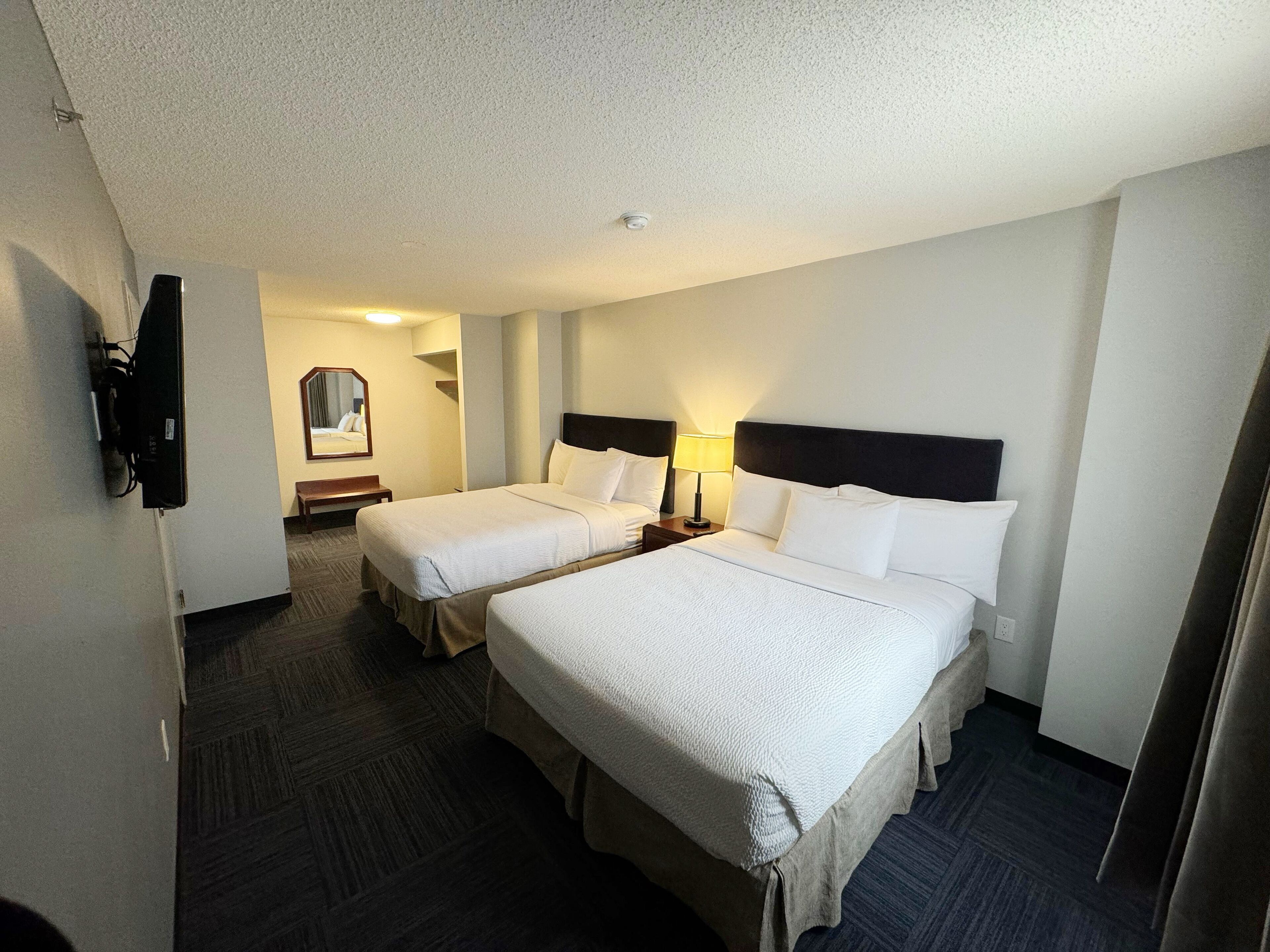 A hotel room with two beds, a TV, a mirror, and a lamp.
