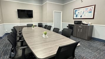 Una sala de conferencias con una mesa larga, sillas, un televisor de pantalla plana, una puerta y un armario con un cuadro enmarcado.
