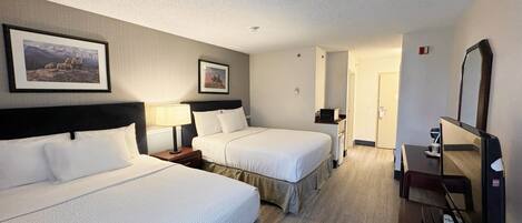 A hotel room with two beds, a TV, a desk, and a door leading to another room.