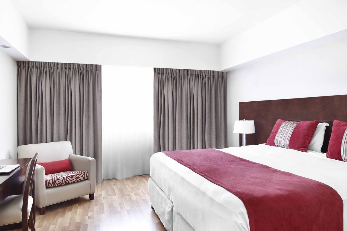 Une chambre d’hôtel avec un lit, une chaise, un bureau et des rideaux.