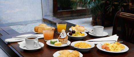 A breakfast table with plates of food, a cup of coffee, and a glass of orange juice.