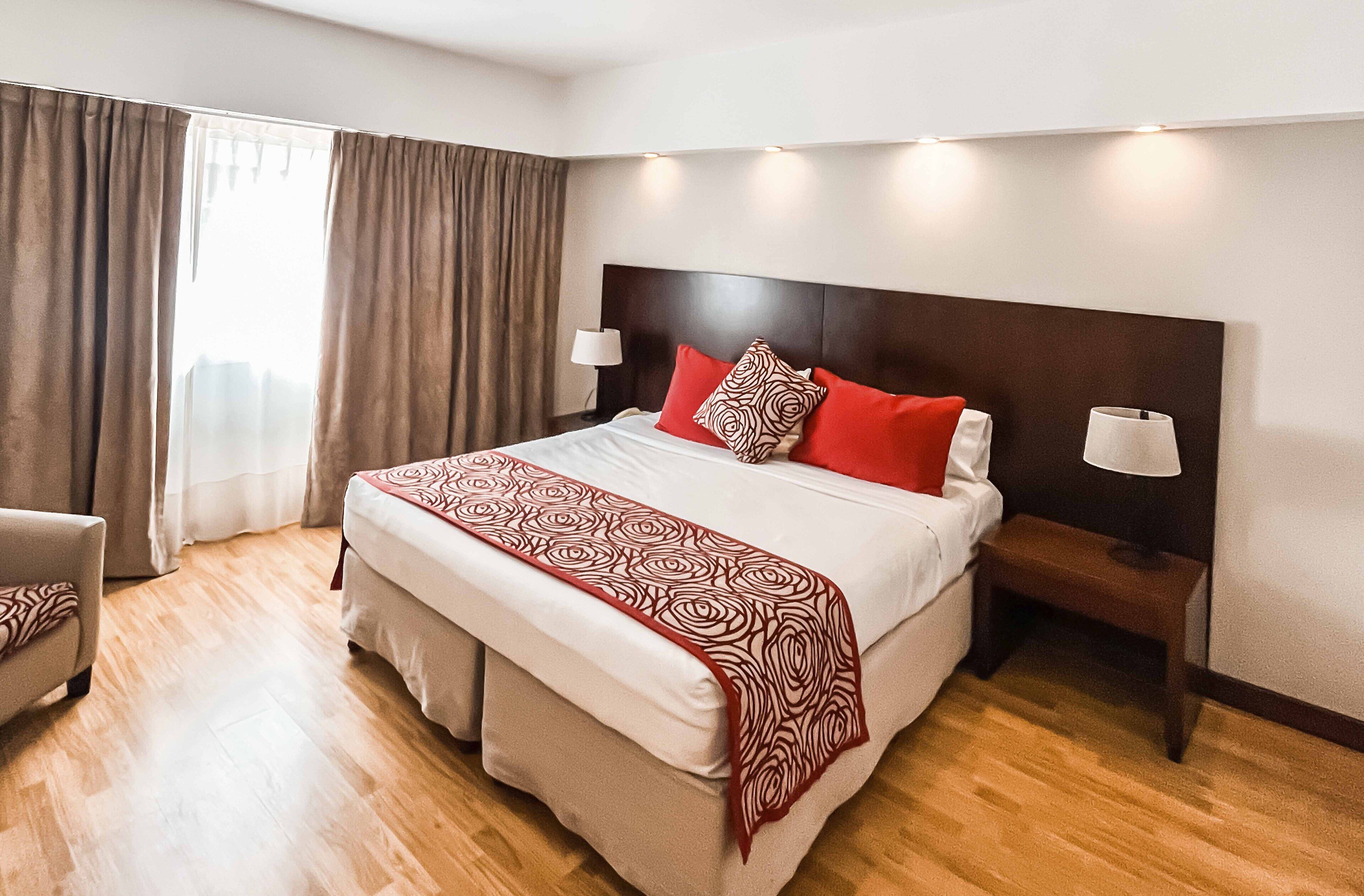 A hotel room with a large bed, two bedside lamps, a chair, and a window with curtains.