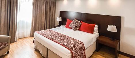 A hotel room with a large bed, two bedside lamps, a chair, and a window with curtains.