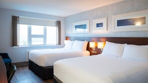 Quarto de hotel com duas camas, uma escrivaninha e uma janela com cortinas.