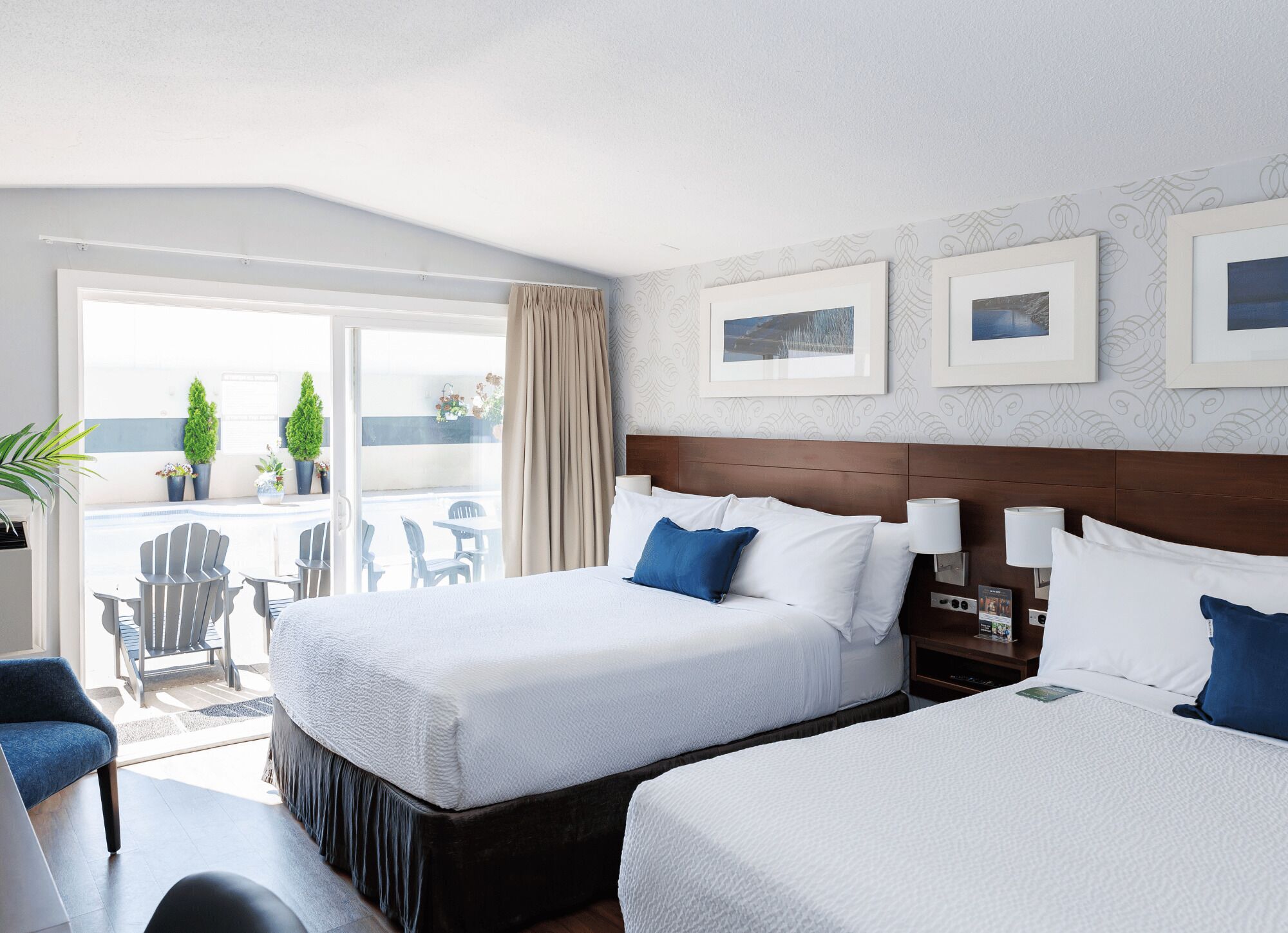 A hotel room with two beds, a balcony with outdoor seating, and framed pictures on the wall.