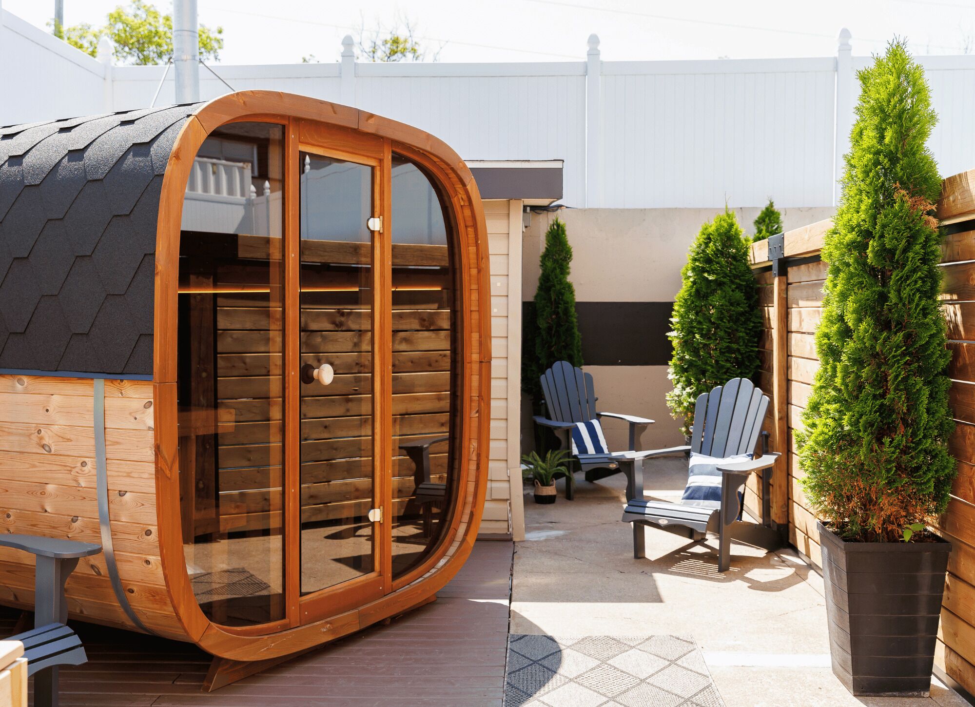 A wooden pod-like structure with a sliding door, adjacent to a patio area with Adirondack chairs and a potted plant.