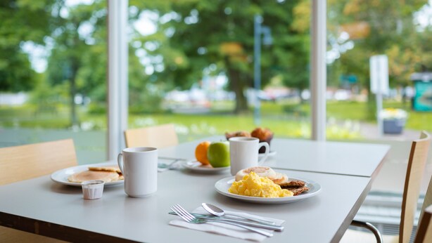 Uma mesa de café da manhã com pratos de comida, uma xícara de café e talheres.