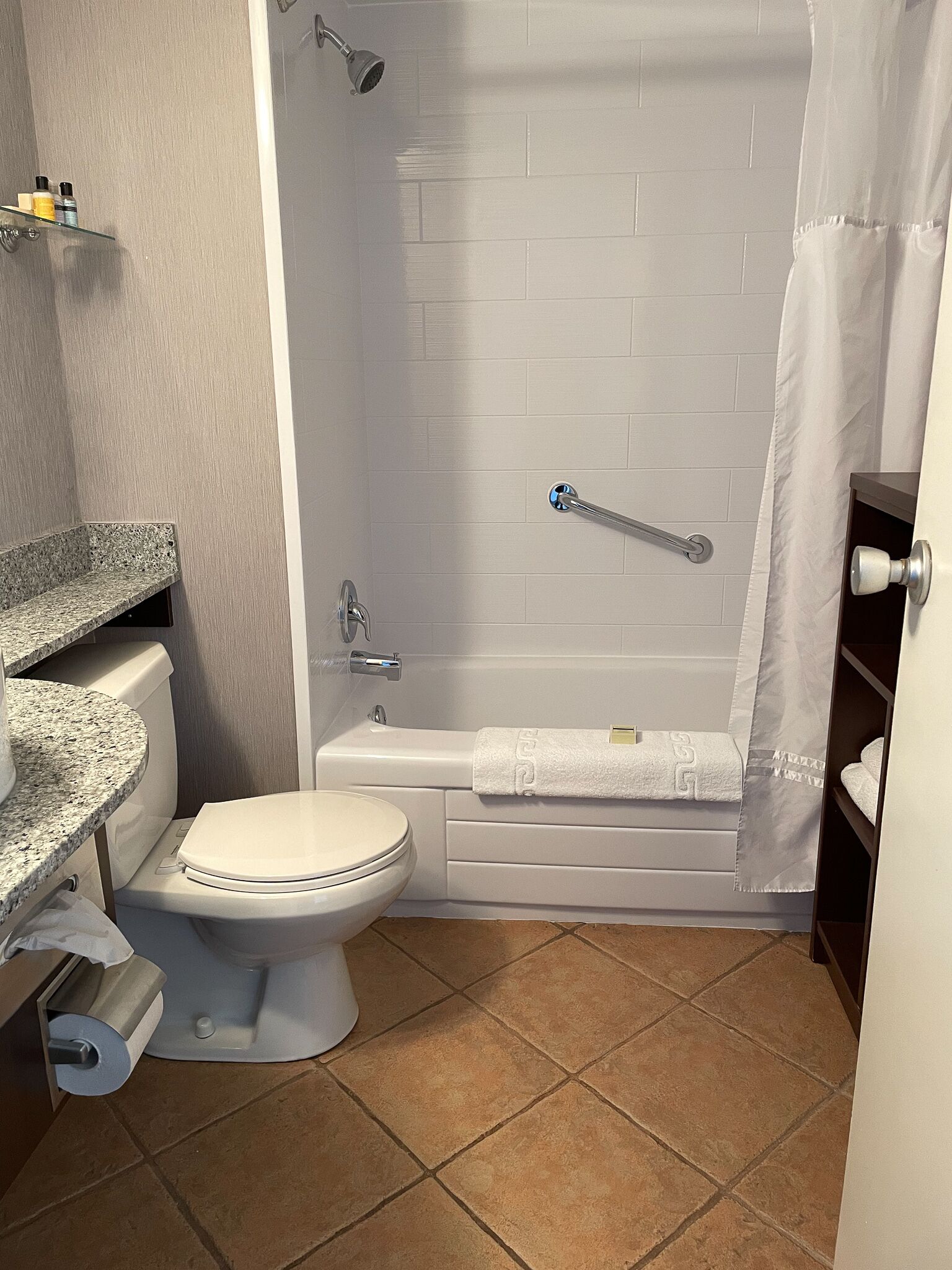 A bathroom with a toilet, a shower with a grab bar, a bathtub, and a sink with a granite countertop.