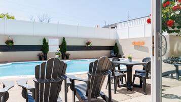 Zona de piscina con sillas Adirondack y mesas, un letrero en la pared y una cerca blanca.