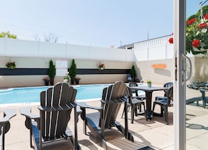 A poolside area with Adirondack chairs and tables, a sign on the wall, and a white fence. - Rodd Moncton Hotel (Moncton)