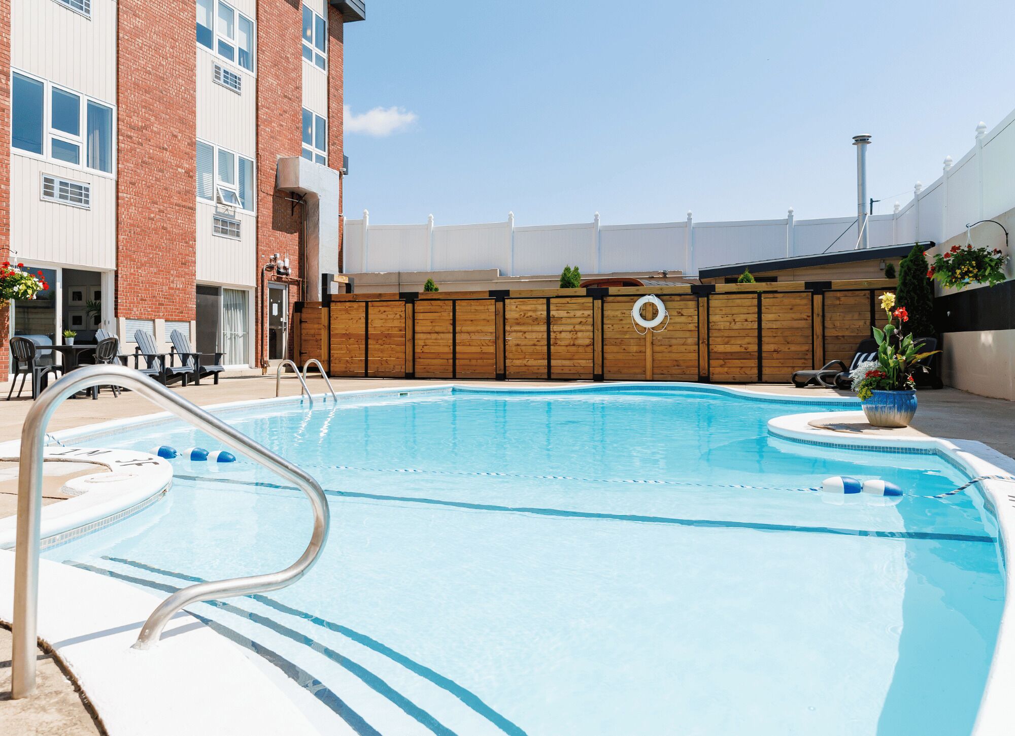Une piscine avec une terrasse en bois, un poste de surveillance pour les sauveteurs et une vue sur un bâtiment doté de fenêtres et d’une porte.