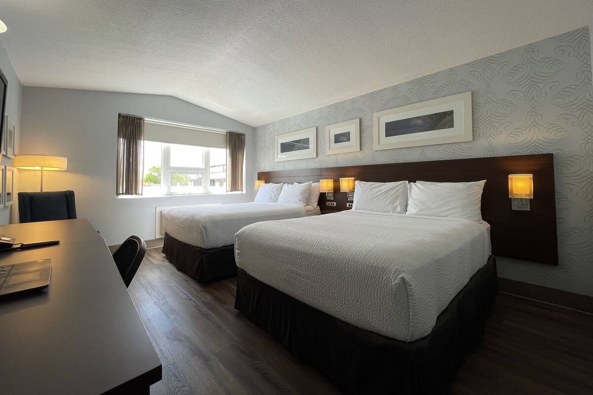 Quarto de hotel com duas camas, uma escrivaninha e uma janela com cortinas.