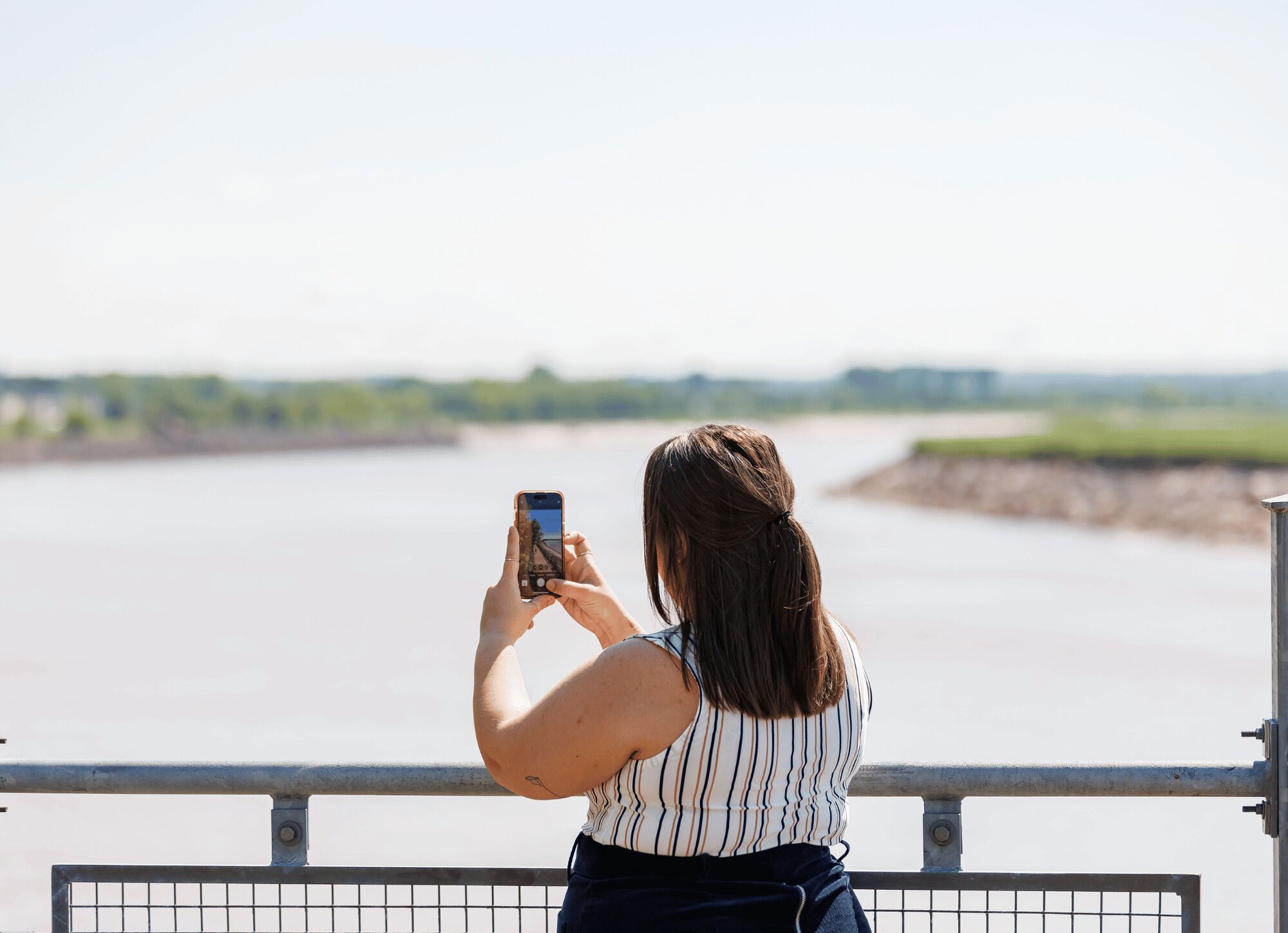 En person fotograferer et flodlandskab fra et gelænder.
