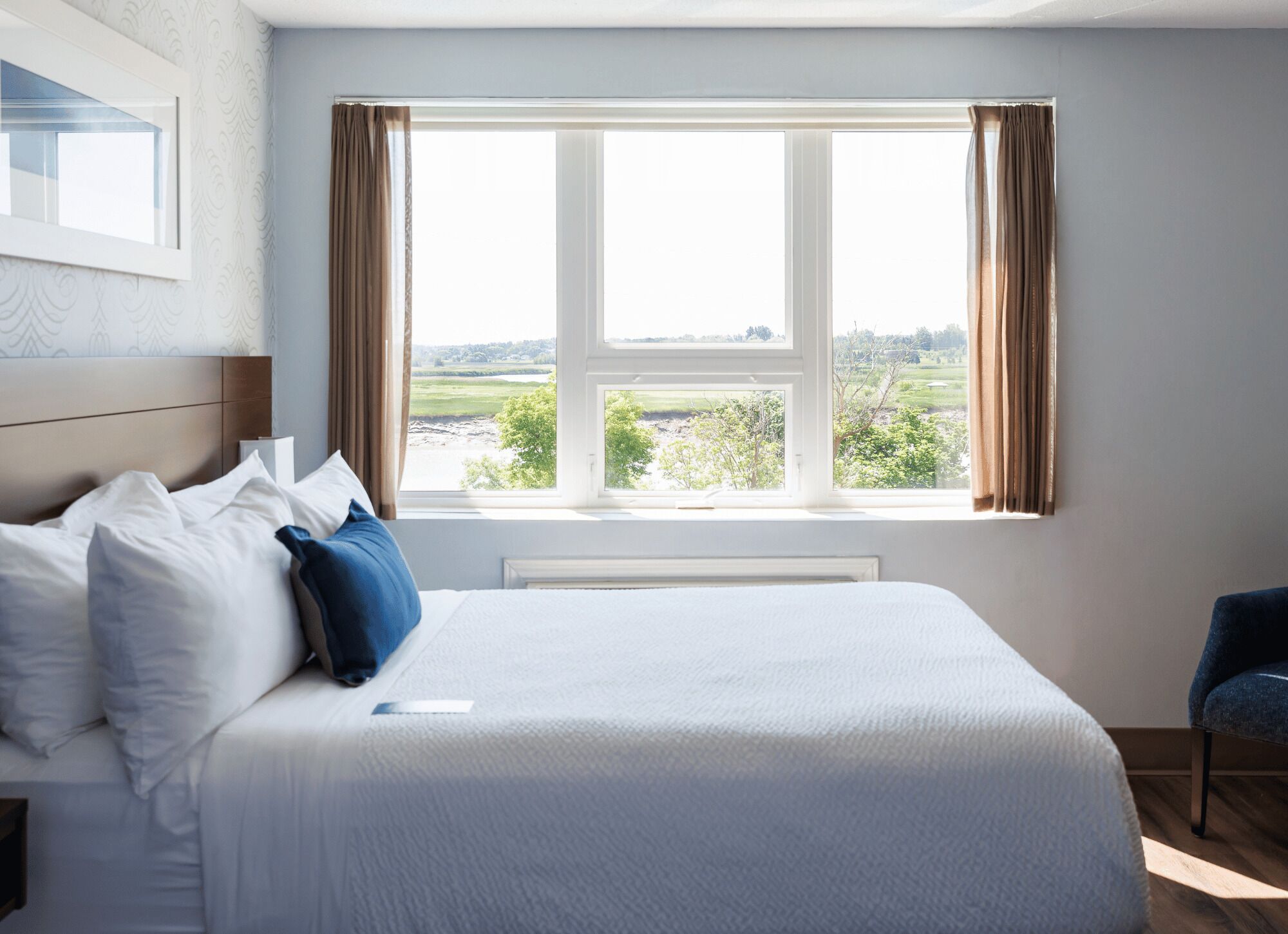 A hotel room with a large bed, a view of the countryside, and a window with curtains.