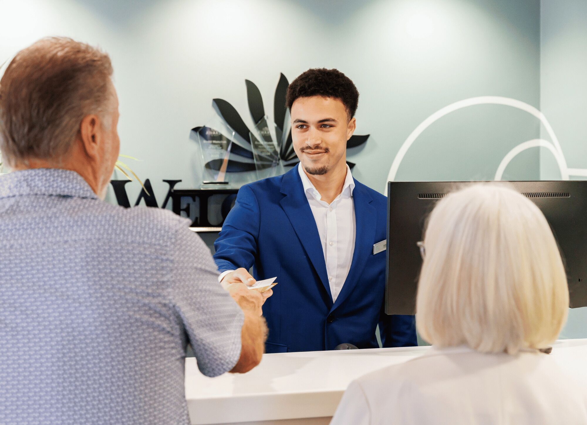 Zona de recepción de un hotel, con una recepcionista, un huésped y un mostrador.