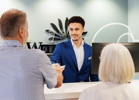 Zona de recepción de un hotel, con una recepcionista, un huésped y un mostrador.