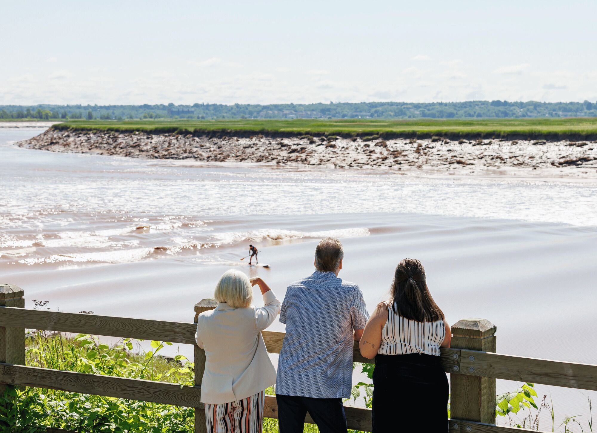 A wooden viewing deck overlooking a river with a sandy beach and a distant rocky shoreline.