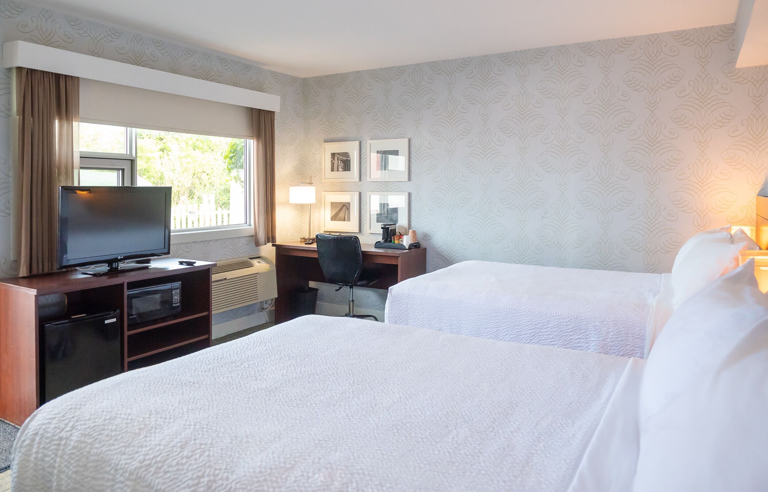 A hotel room with two beds, a desk, a television, and a window with curtains.