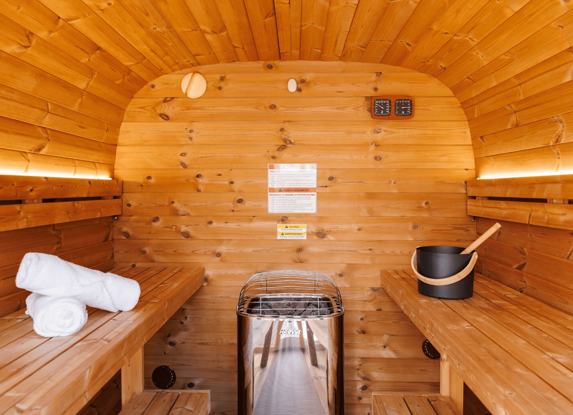 A sauna with wooden walls, benches, a towel, a sauna heater, and a pot.