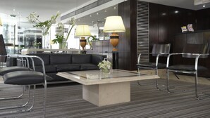 Un espace d’attente moderne comprenant un canapé, des fauteuils, une table basse et deux lampes.