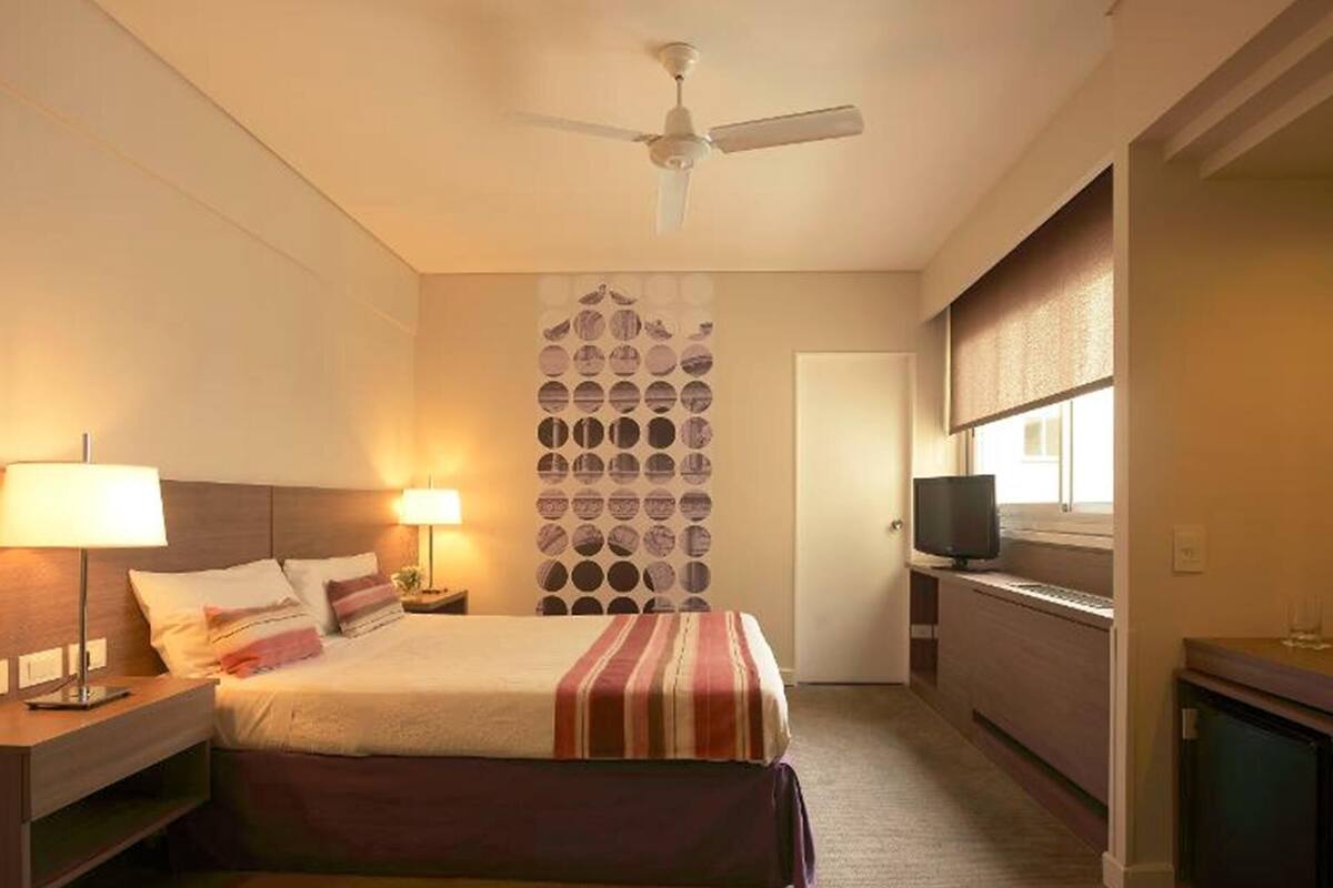 Una camera d'albergo con un letto, abat-jour, una ventola a soffitto, una TV e una parete con decorazioni circolari.