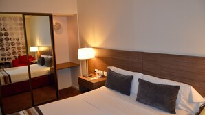 Une chambre d’hôtel avec un lit, une table de chevet, une lampe, un miroir et une chaise rouge.