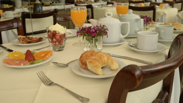 Une table mise pour le petit-déjeuner, avec des assiettes remplies de nourriture, un croissant, des fruits et un vase de fleurs.