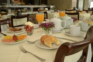 Desayuno con platos de comida, un croissant, fruta y un jarrón de flores.