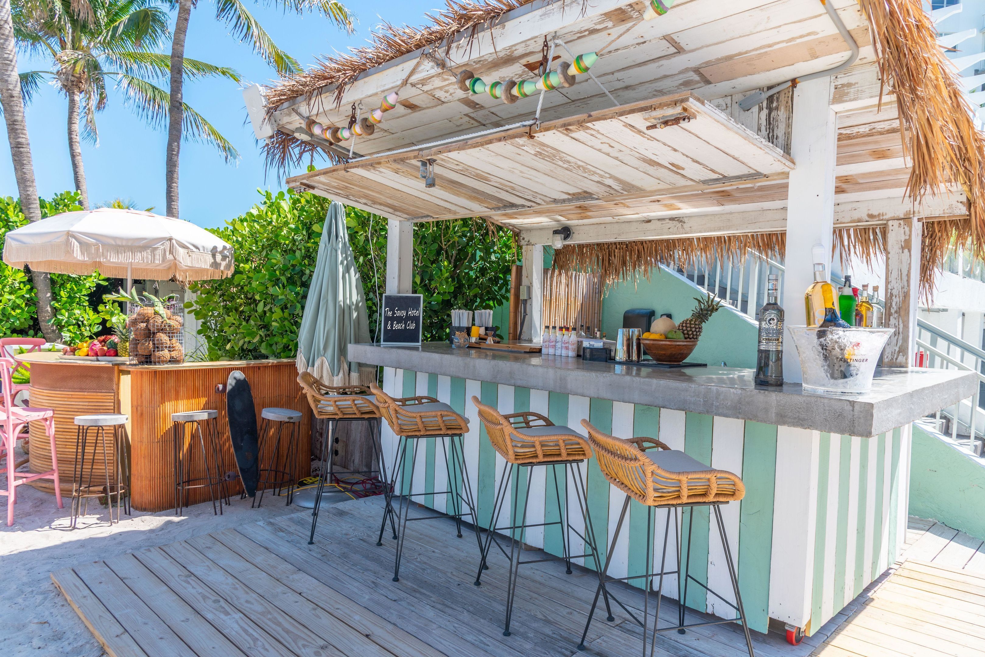 Eine Strandbar mit einer Holzterrasse, einer gestreiften Bar und Korbstühlen.