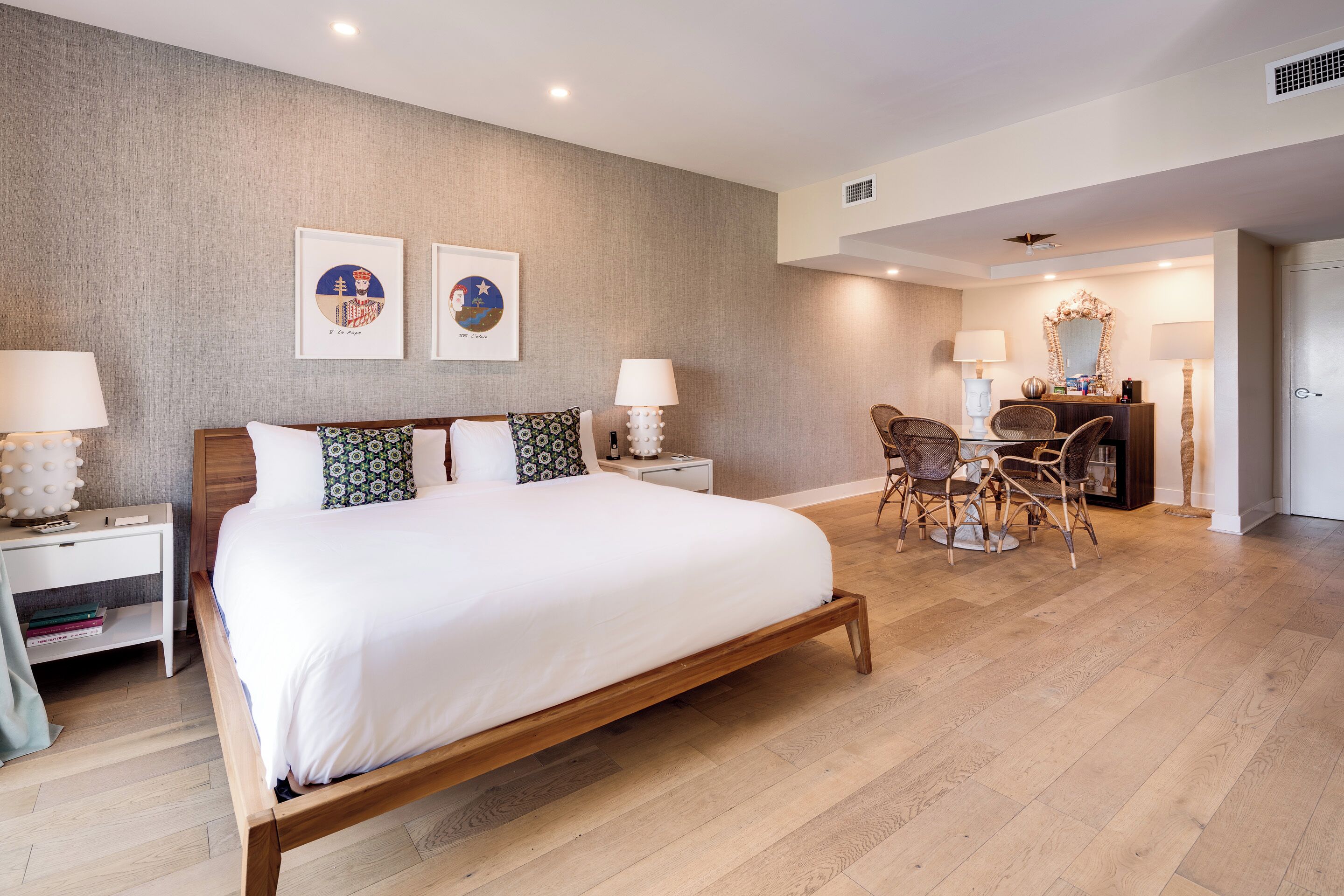 A spacious bedroom with a large bed, bedside tables with lamps, a desk with chairs, and a mirror.