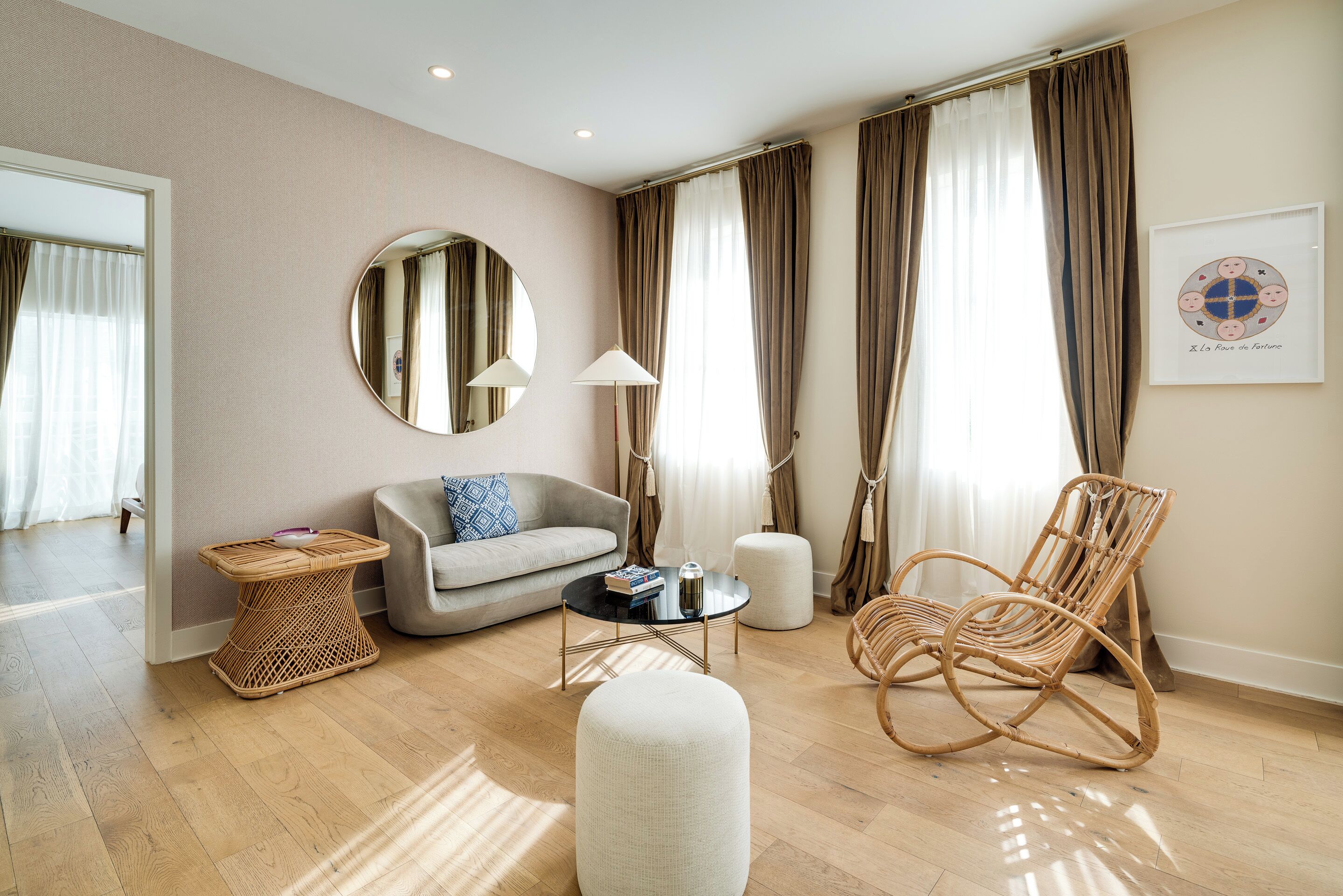 A modern living room with a sofa, round coffee table, wicker chair, and a large mirror.