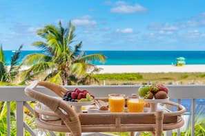 A wicker tray with breakfast items and a view of a beach and ocean. - The Savoy Hotel & Beach Club (Miami Beach)