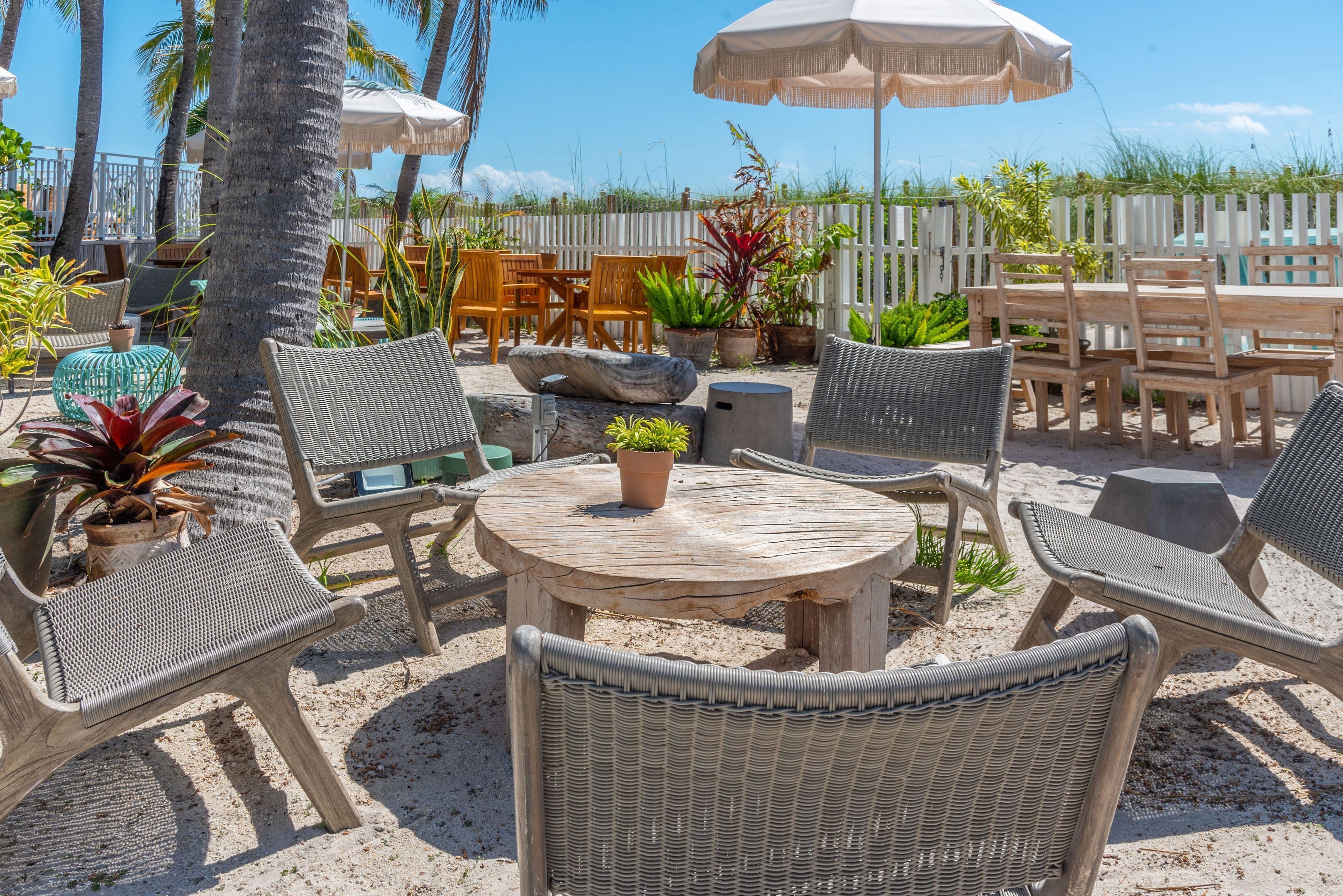Ein Patio mit Korbmöbeln, einem runden Holztisch und Topfpflanzen.