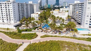 A high-rise hotel with multiple balconies, a pool area with umbrellas, and a view of the city skyline. - The Savoy Hotel & Beach Club (Miami Beach)